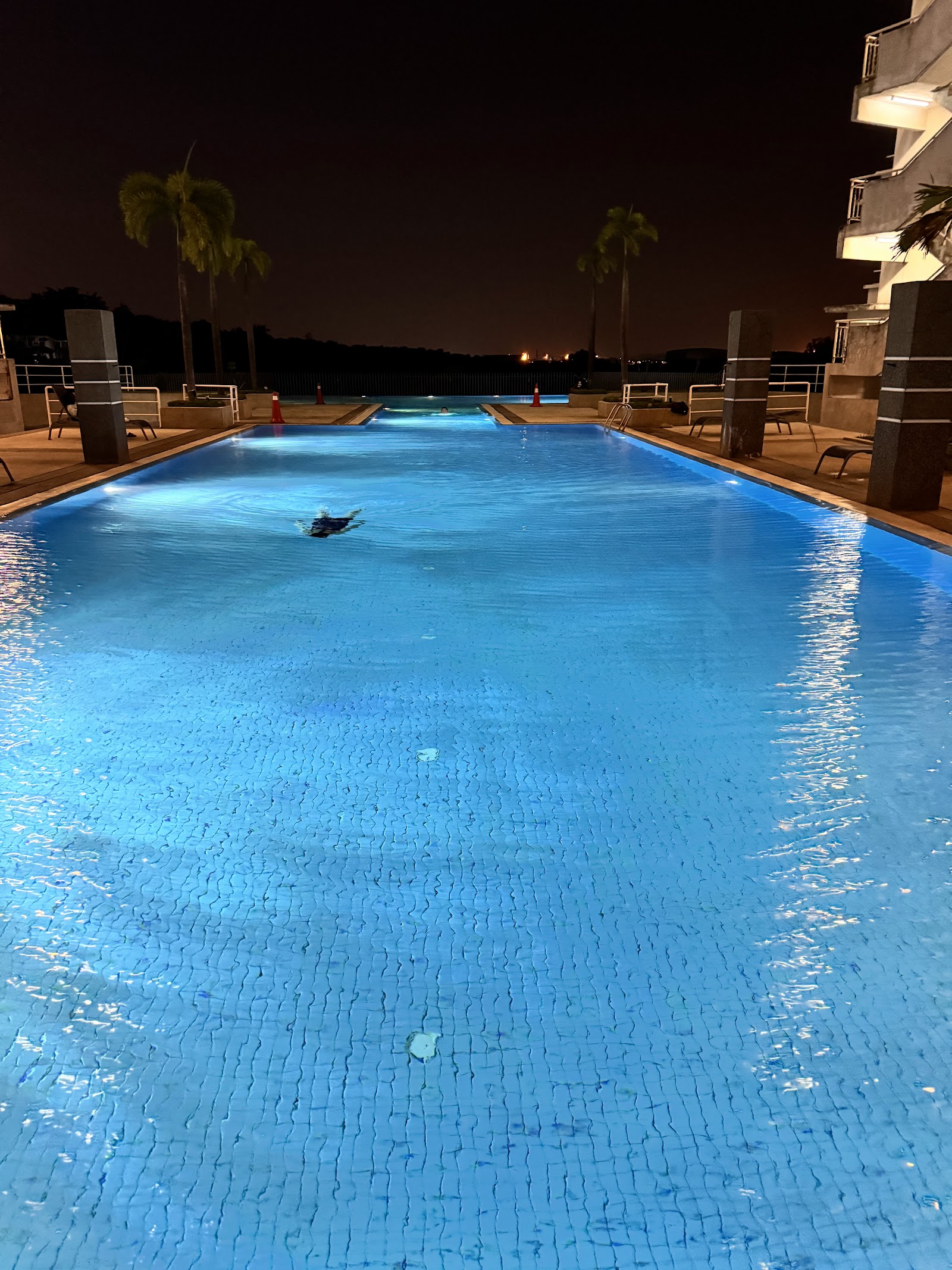 Cova Suites: A swimming pool illuminated at night, with a person swimming and palm trees in the background.