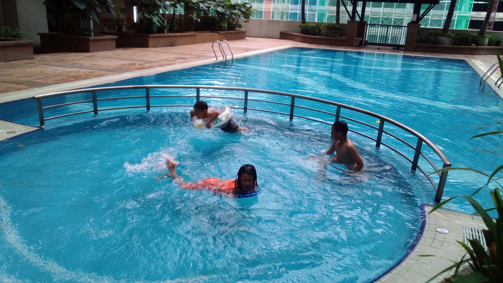 Residensi Laguna: People swimming in a circular pool section of a resort pool, with a surrounding deck and buildings in the background.