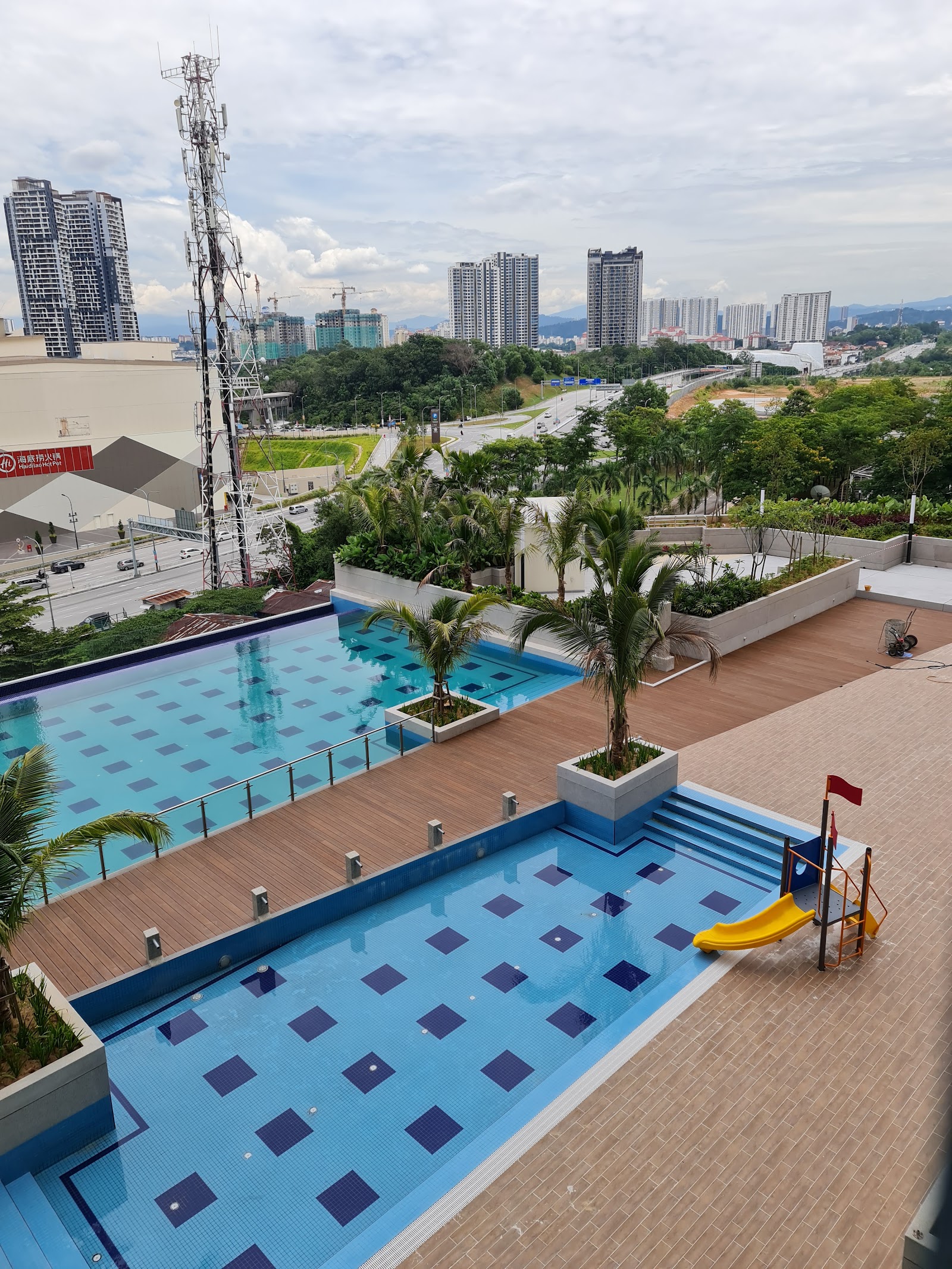 Paraiso Residence: A rooftop swimming pool area with a children's play pool and slide, overlooking a city with skyscrapers and a communication tower.