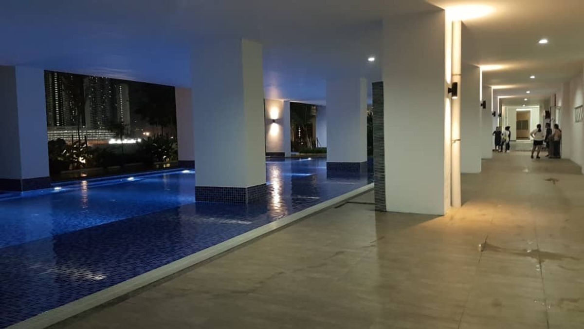 Residensi Puchongmas: A covered walkway with a swimming pool on the left and columns along the side, with people in the distance.