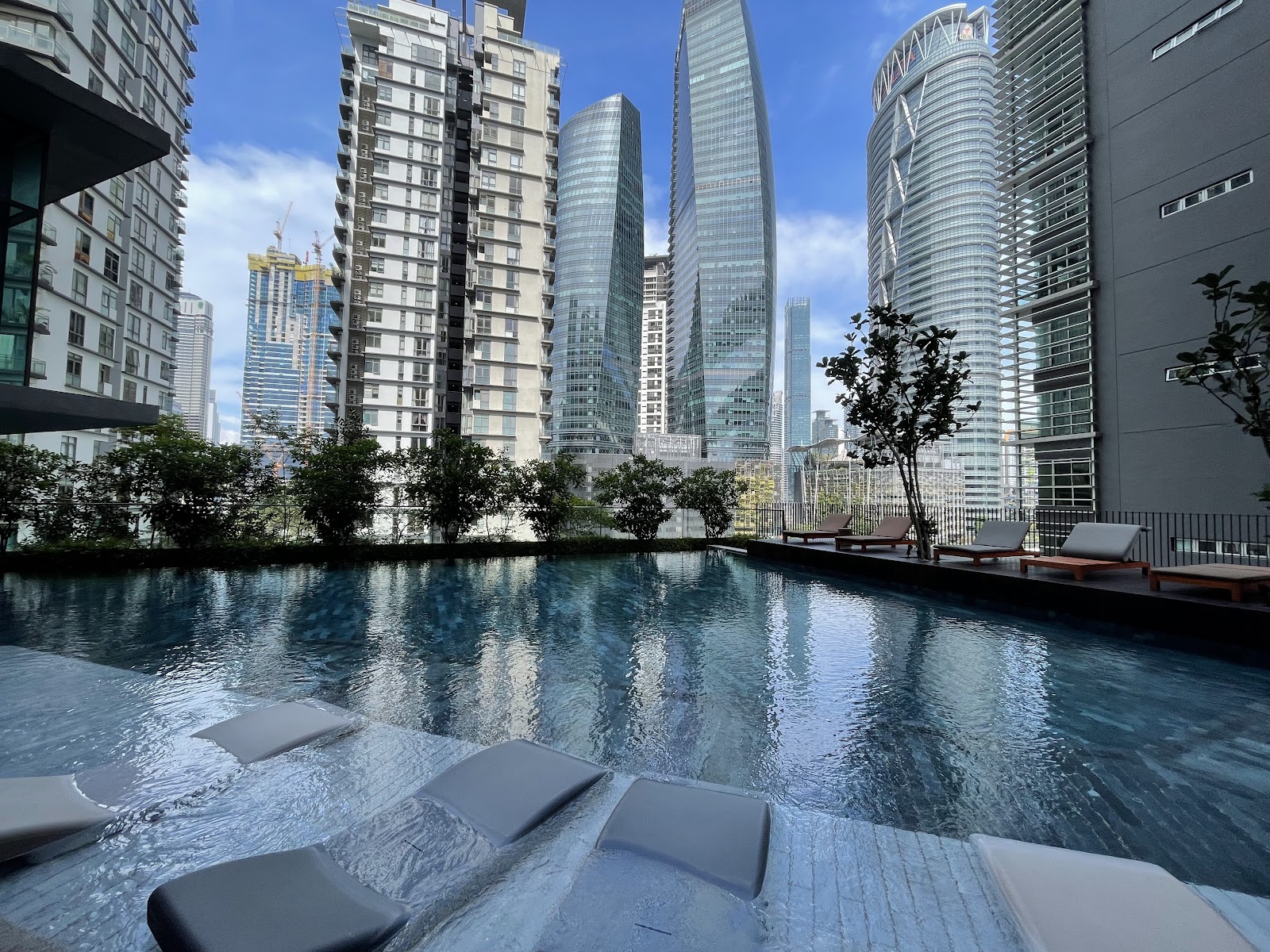 Stonor 3: An outdoor swimming pool with lounge chairs and small trees, surrounded by high-rise residential towers under a blue sky.