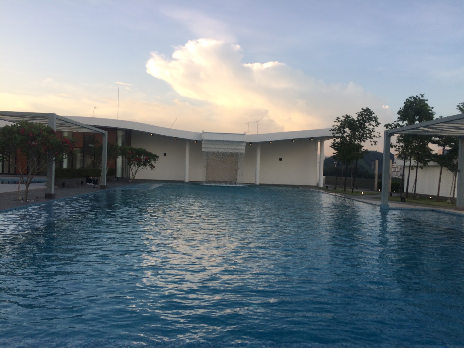 Encorp Strand Residences: An outdoor swimming pool at dusk featuring a large water feature on the far end, surrounded by trees and covered walkways.