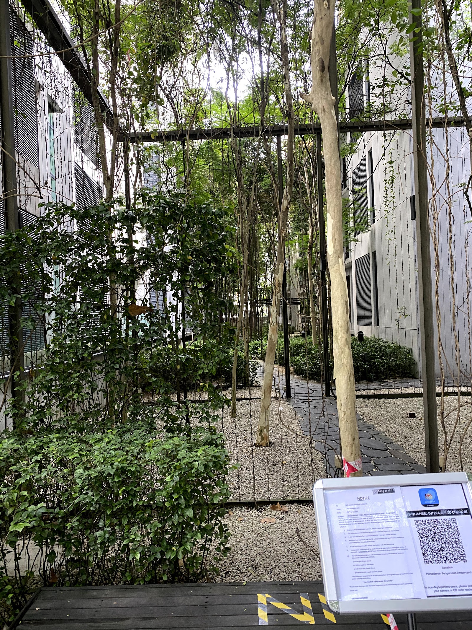 Ampersand: A landscaped garden area with a tree-lined path and notice boards in the foreground.