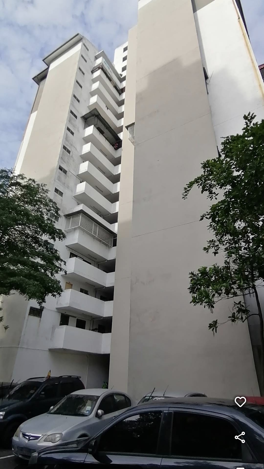 Apartment Seri Ceria 1: A low-angle view of a white high-rise apartment building exterior with parked cars at the base and trees flanking the scene.