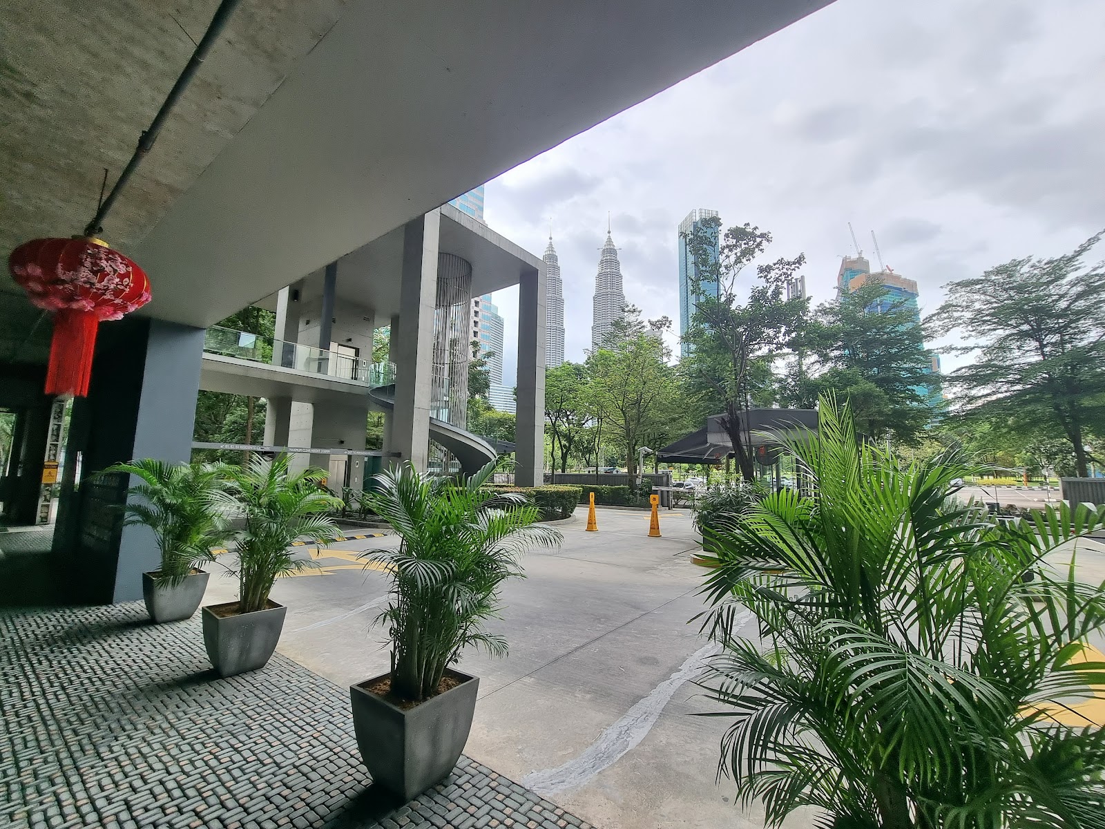 Park Seven: A covered driveway entrance of a modern complex with potted plants, red lanterns, and a view of the Petronas Twin Towers in the background.