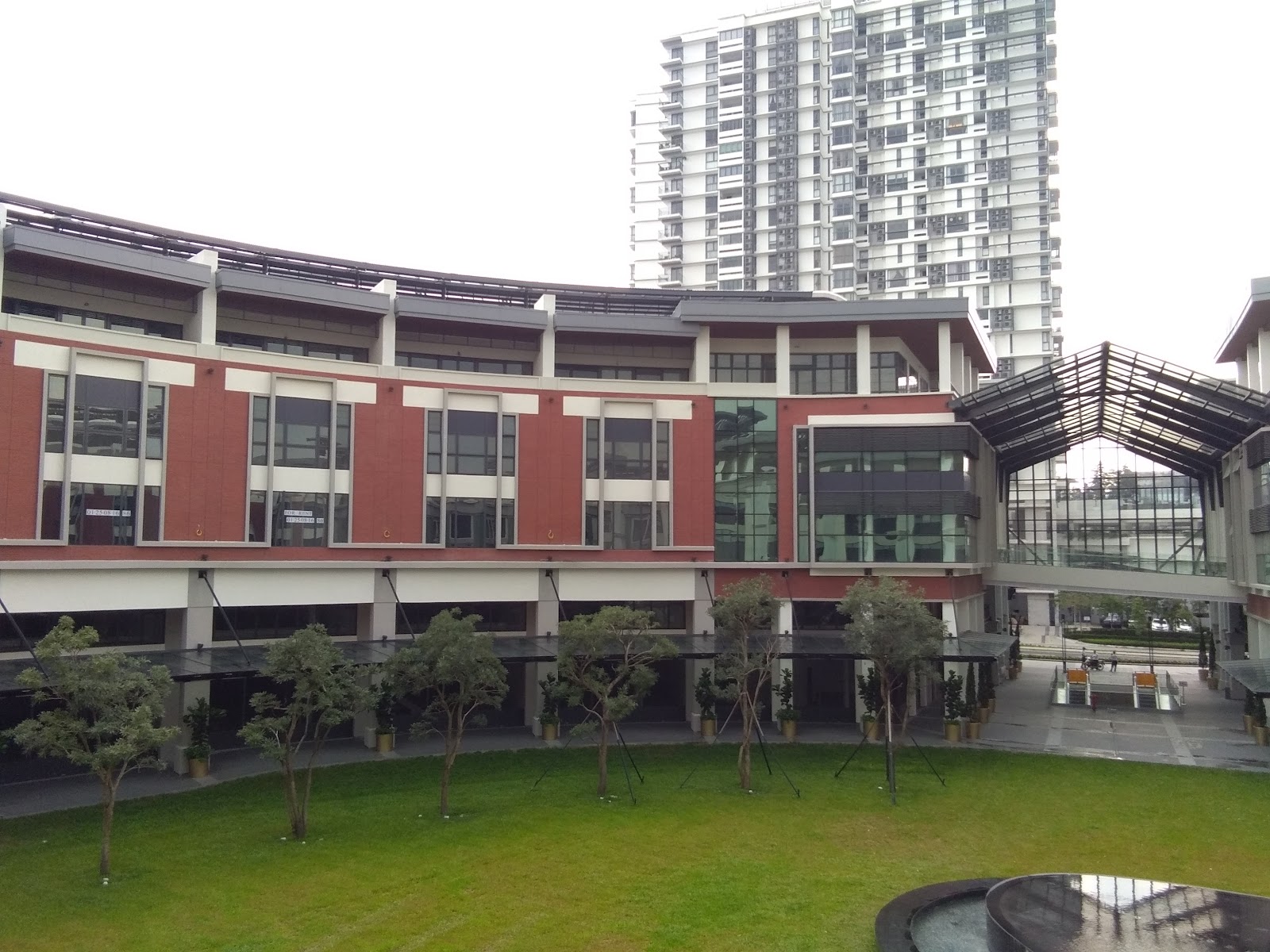 The BreezeWay Garden: The exterior of a building with a red brick facade and glass windows, featuring a landscaped garden with small trees and a modern canopy structure, with a high-rise tower in the background.