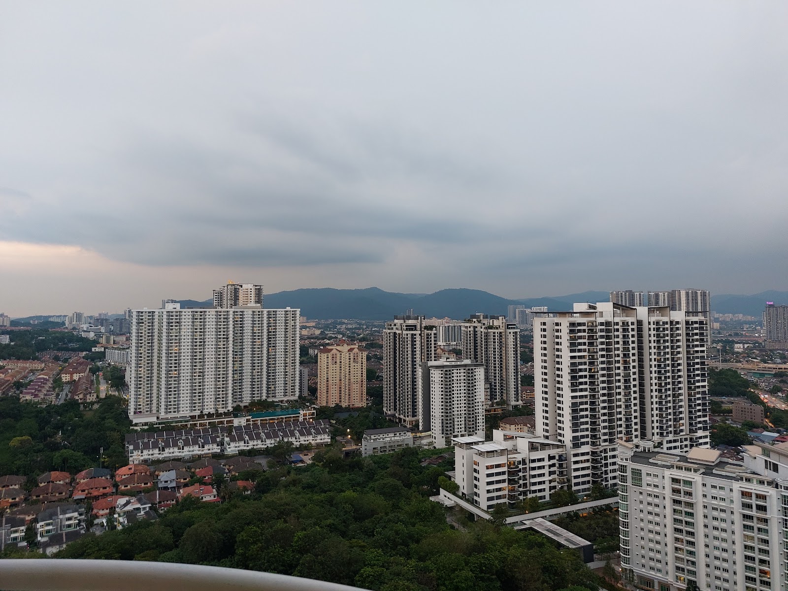 Duta Ria: A panoramic view from a high vantage point overlooking a dense residential area with multiple apartment towers and distant hills under a cloudy sky.