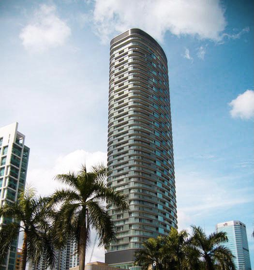 K Residence: A finished, cylindrical high-rise tower with a dark glass facade stands against a blue sky, framed by palm trees and adjacent buildings.