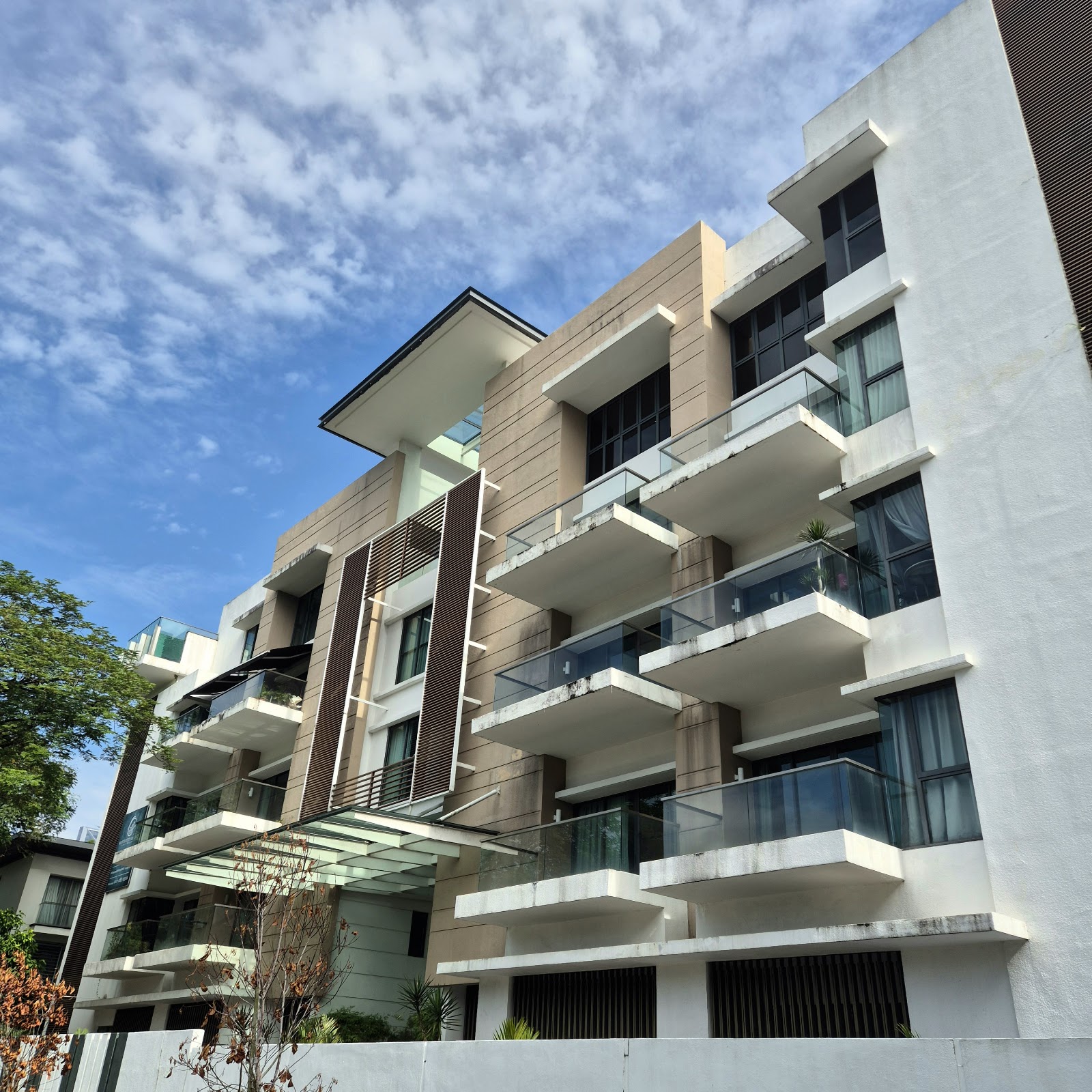 Identiti U-Thant: Low-angle view of the exterior facade of a modern condominium building with balconies, looking up against a blue sky with scattered clouds.