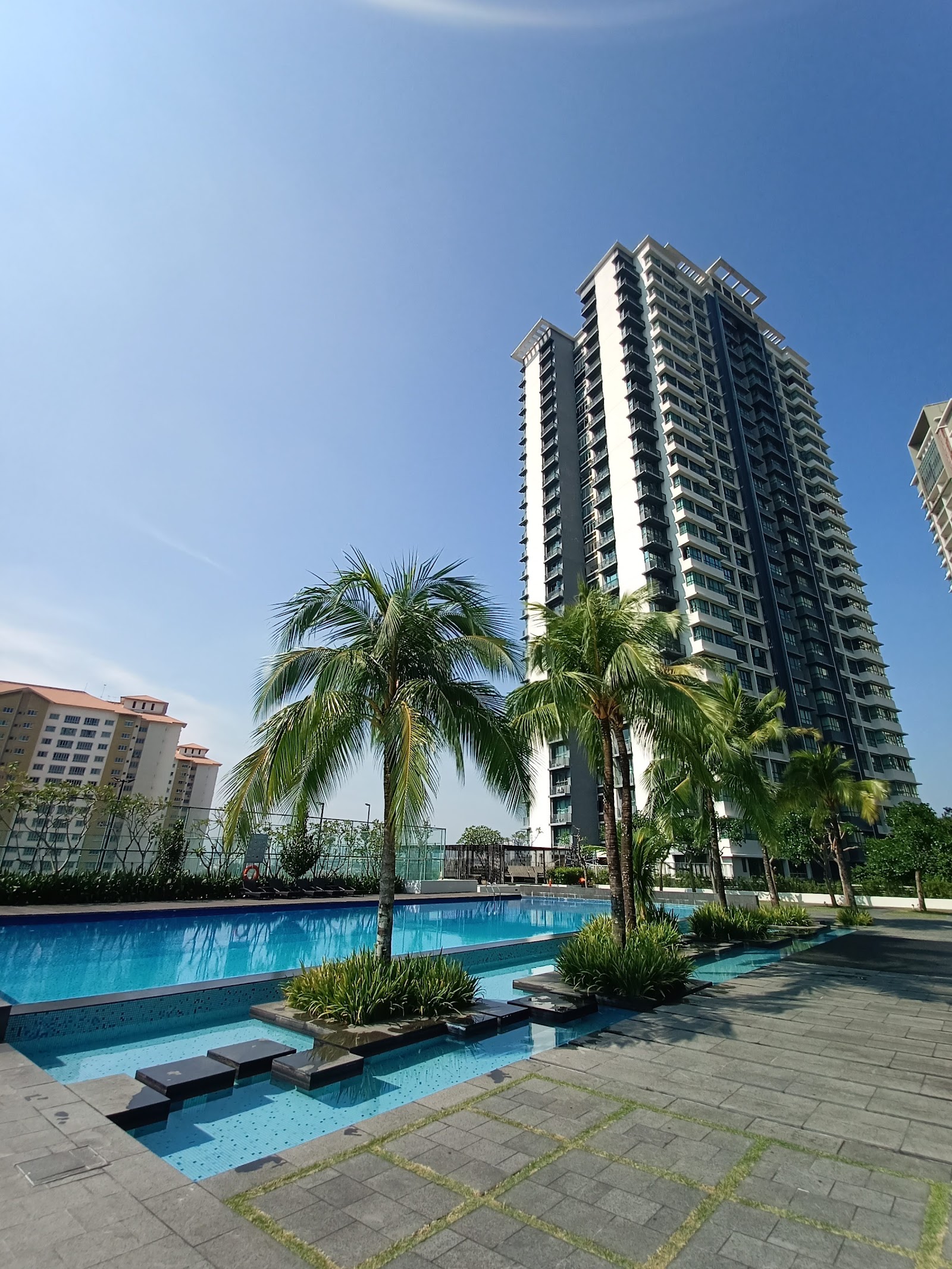 KM1: A modern swimming pool deck with palm trees and landscaping, with a high-rise residential tower in the background.