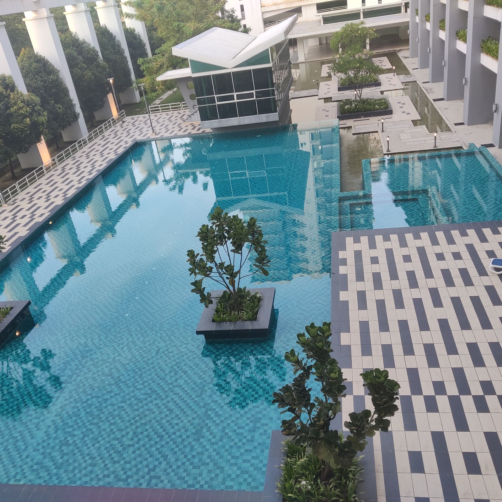 Kiara Residence 1: Overhead view of an outdoor swimming pool with a small planter in the center, surrounded by tiled decks and landscaping.
