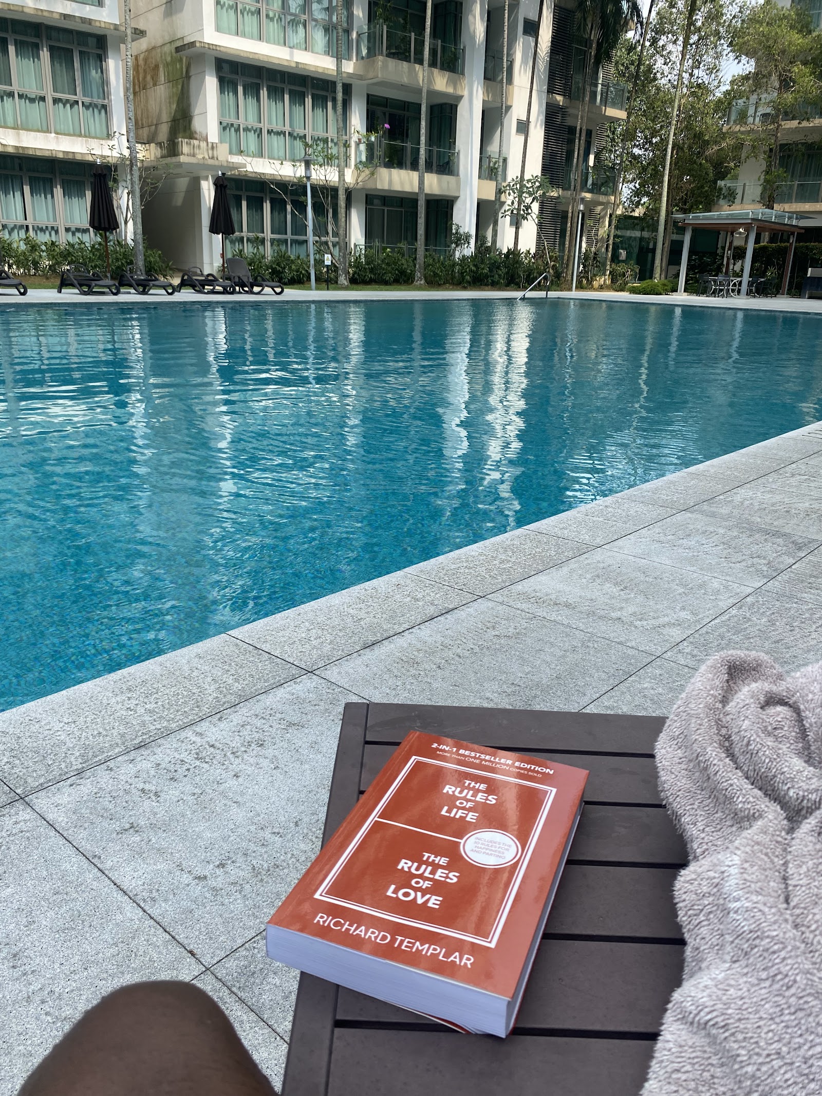 Seri Hening Residence: A book titled 'The Rules of Life and Love' by Richard Templar rests on a table next to a swimming pool.