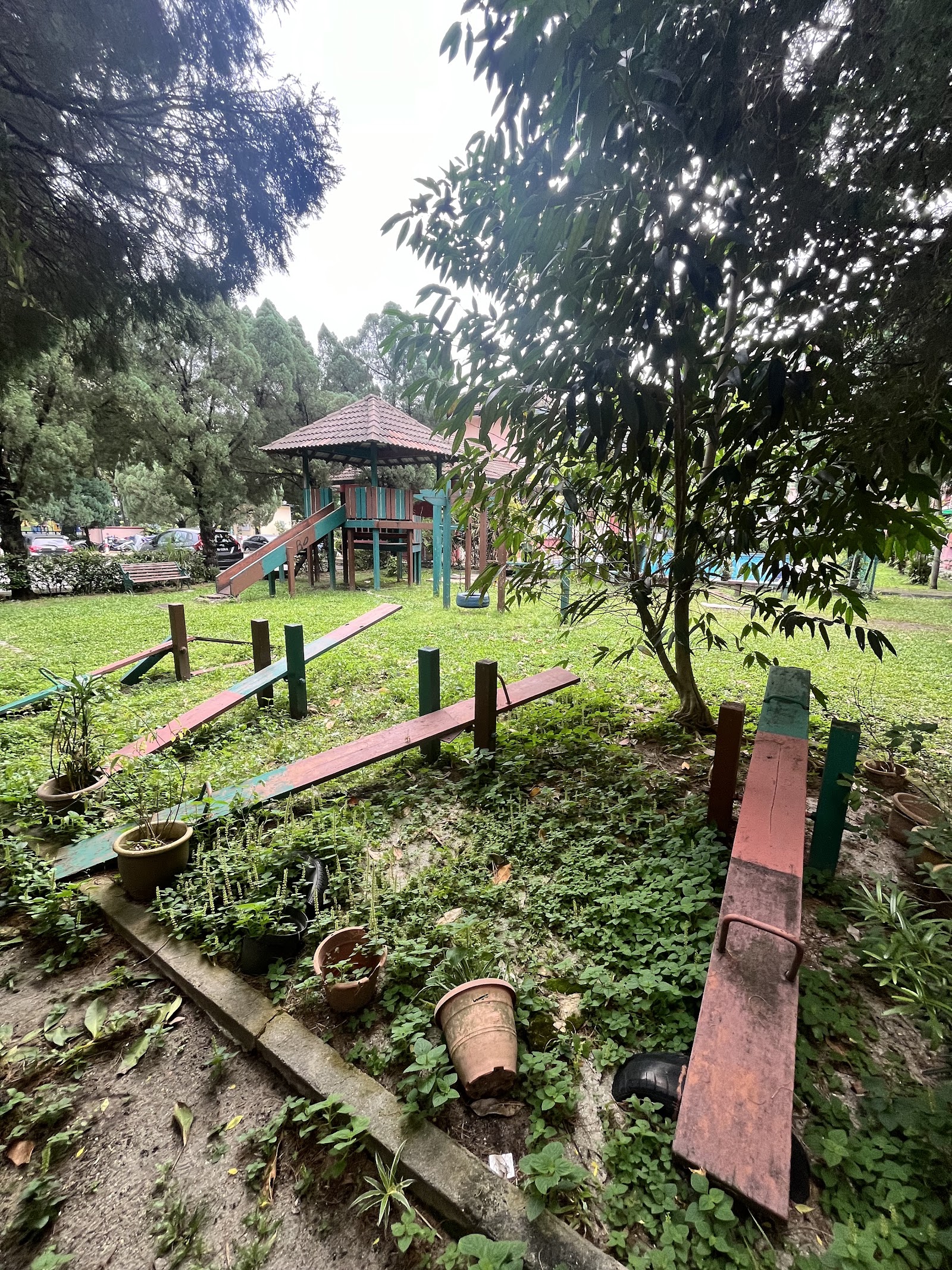 Pangsapuri Kayangan: A playground area featuring wooden seesaws and a play structure with a slide, set in a grassy garden.