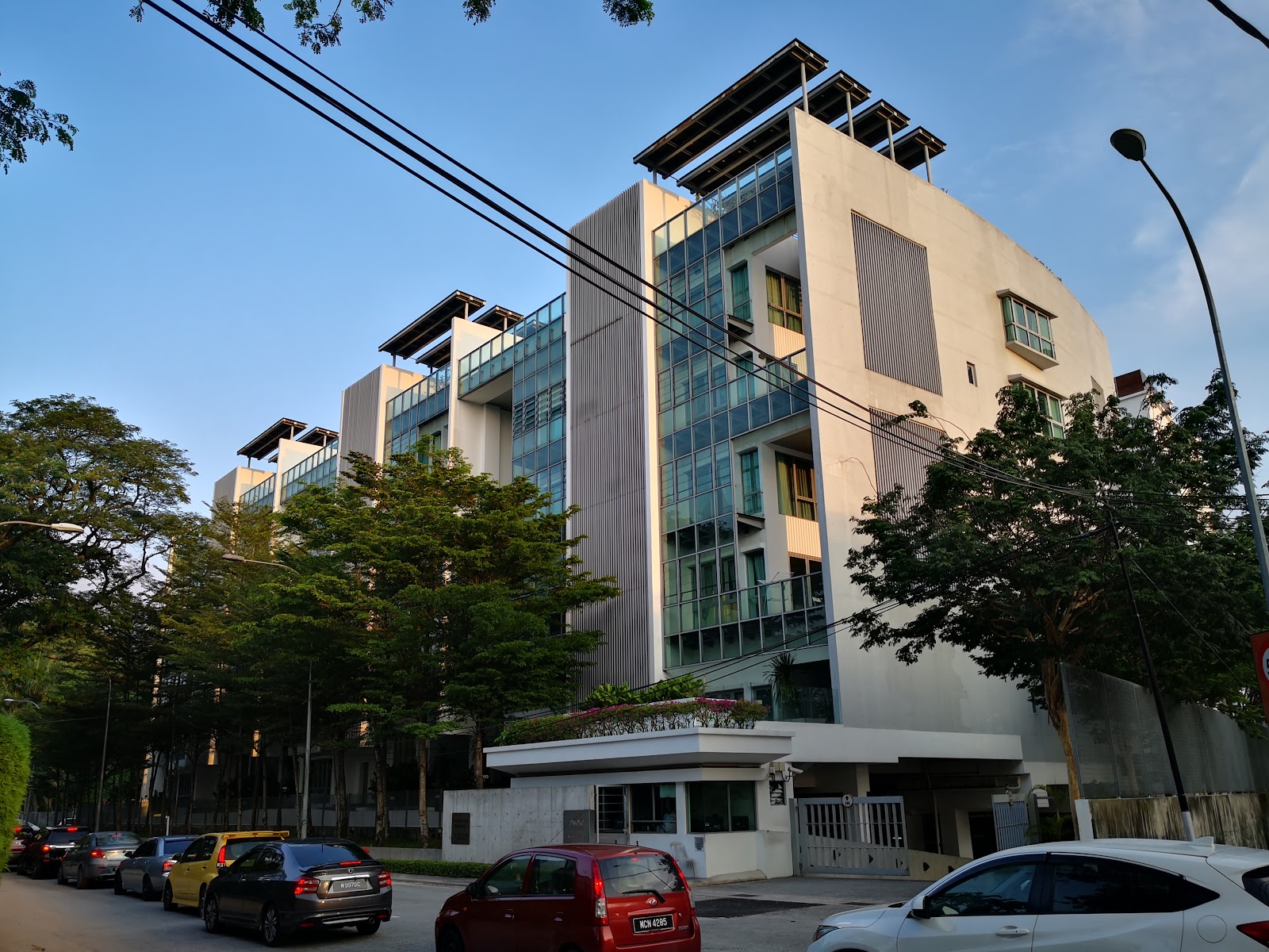 Amarin Wickham: A view of the exterior facade of a modern multi-story residential building with a street and parked cars in the foreground.