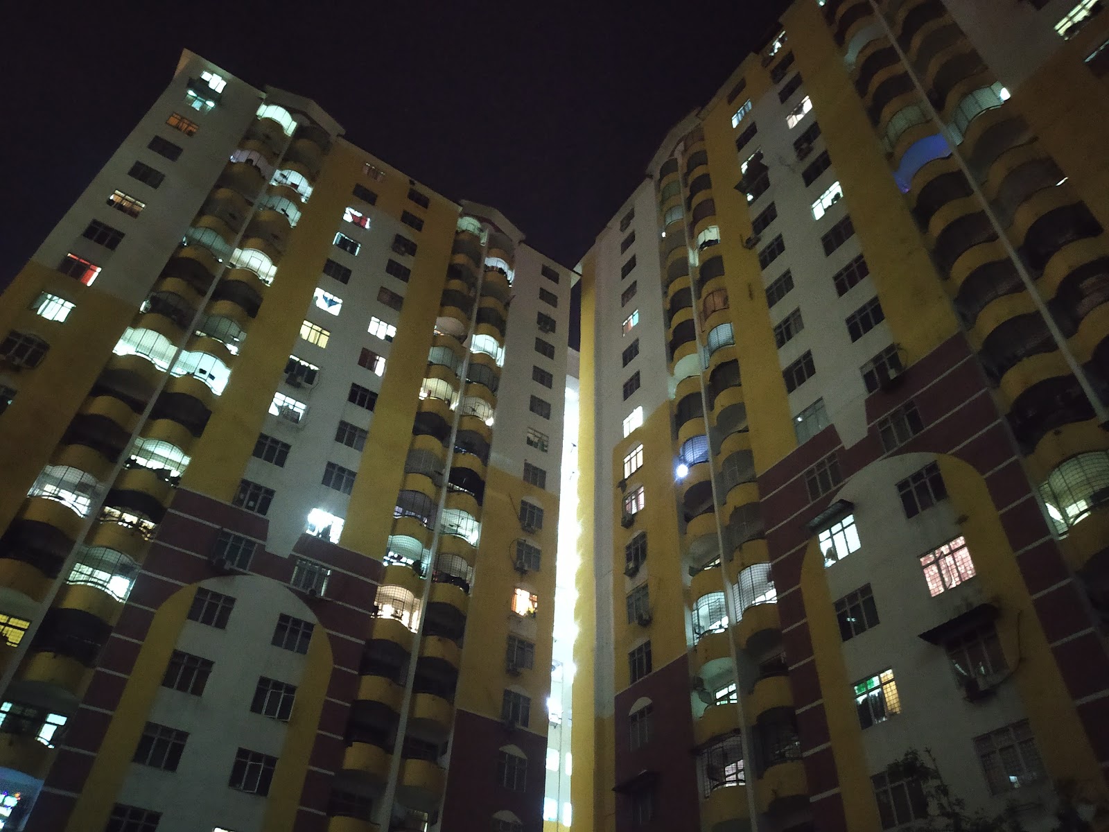 Lagoon Perdana: Two high-rise residential buildings with yellow and white facades and curved balconies, viewed from a low angle at night.