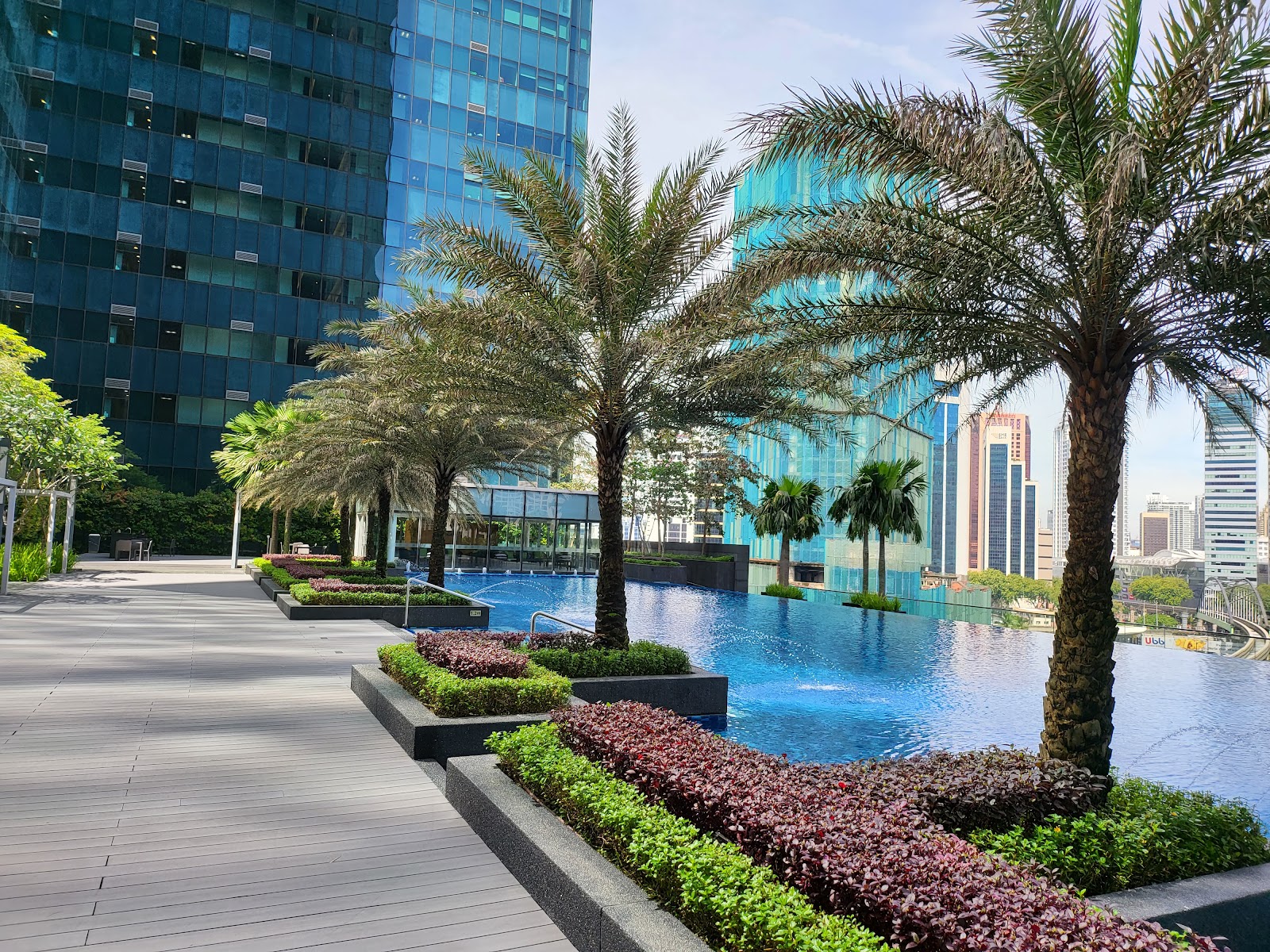 The Ritz-Carlton Residences, Kuala Lumpur: A rooftop infinity pool with palm trees and landscaped planters, set against a backdrop of modern skyscrapers.