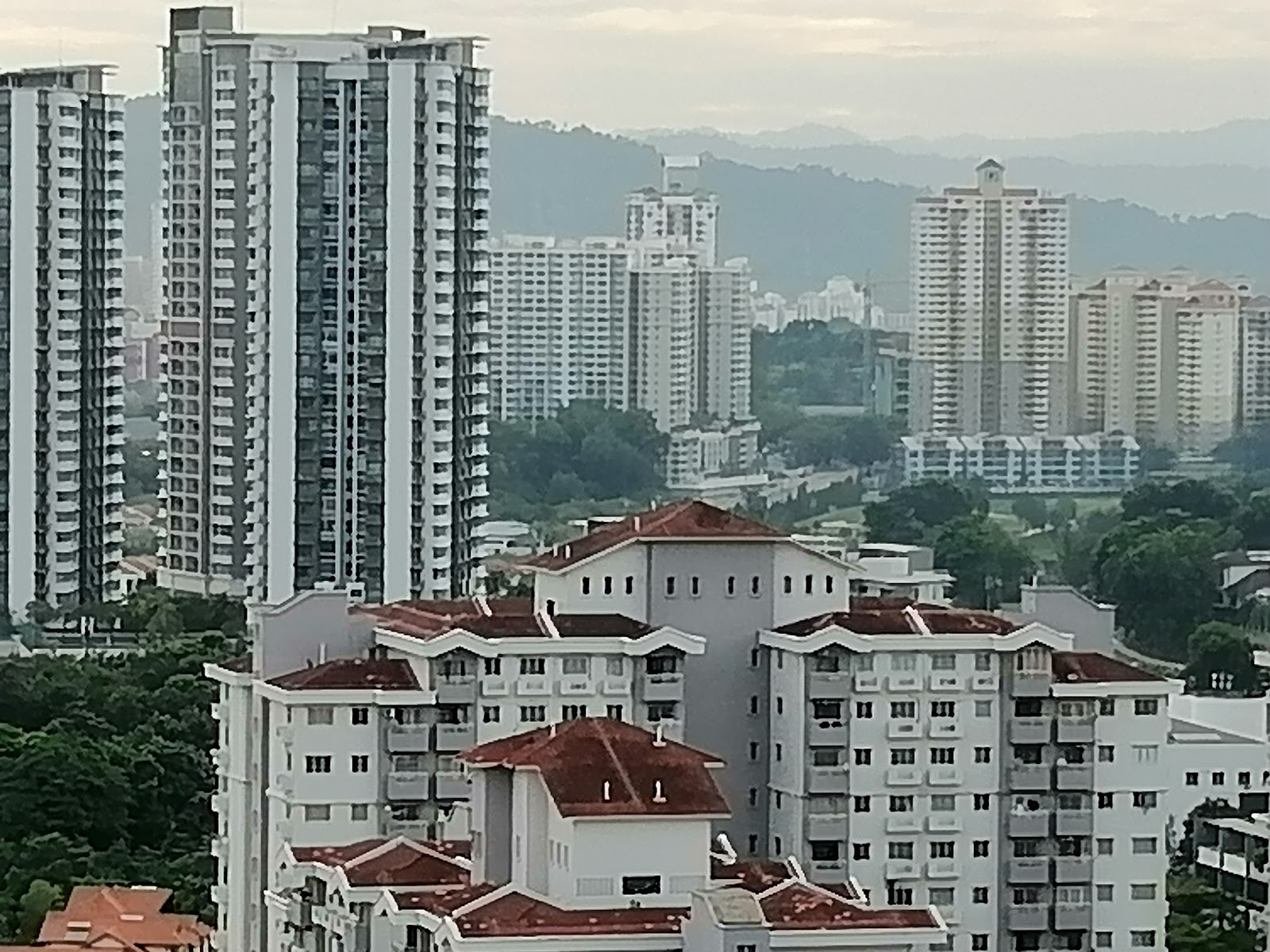 The Havre @ Bukit Jalil: A distant view of a cityscape with modern high-rise apartments and a lower residential building with a red roof, looking towards hills in the background.
