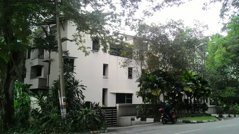 78 LAD: A white multi-story residential building surrounded by trees and landscaping with a motorcyclist on the adjacent road.