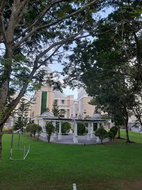 Cova Villa: A view of a large, light-colored building with domes and pillars, seen through the branches of trees in a green garden.