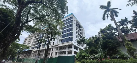Impression U-Thant: The exterior of a high-rise apartment building with a white facade, featuring large trees and vegetation in the foreground.