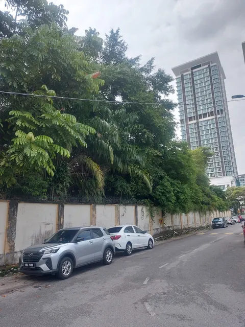 The Spectrum: A street view showing a tall residential tower rising above a wall lined with dense trees and parked cars.