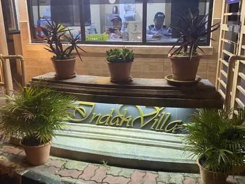Indah Villa: The exterior entrance sign for 'Indah Villa' with potted plants, behind which security guards are visible in a guard house.