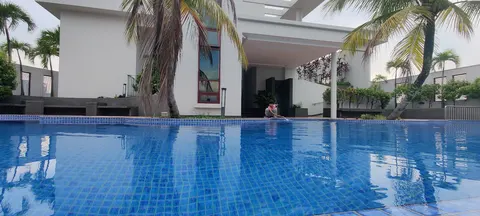 Mutiara Residency: A person cleans the edge of a large blue tiled swimming pool located in the grounds of a modern white building with palm trees.
