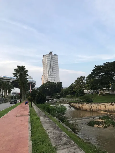 Casa Residenza @ Kota Damansara: A street-level view of a high-rise residential tower with a paved walkway, palm trees, and a small creek with a bridge in the foreground.