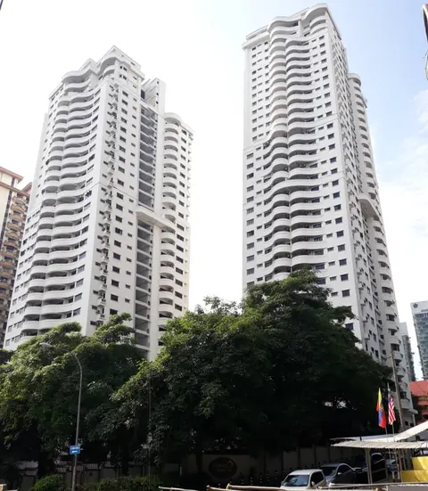 Angkasa Impian 2: A low-angle view of two white residential towers, Angkasa Impian 2, with wavy balconies, framed by lush green trees and a Malaysian flag in the foreground.