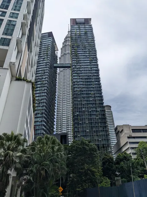 The Meritz: A low-angle street view of tall modern residential towers with vertical greenery on their facades, set against an overcast sky and framed by foreground trees.