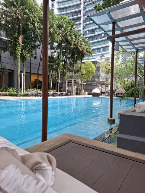 Hampshire Residences: A view of a residential swimming pool area with lounge chairs and palm trees, seen from a shaded deck with an umbrella stand.