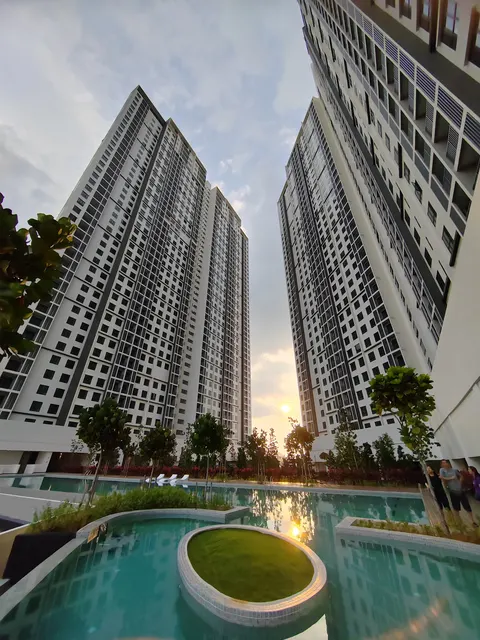 Residensi Bintang Bukit Jalil: A swimming pool and landscaped garden with a circular planter, set within the grounds of a residential development with high-rise towers in the background at sunset.