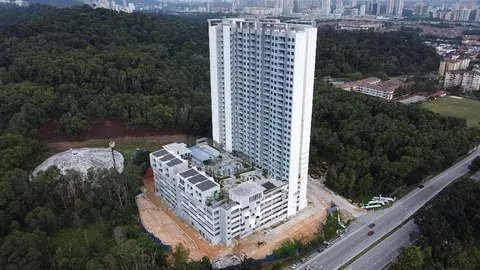 Mahogany Residences: An aerial view of a completed white high-rise tower and its low-rise annex, situated on a hillside next to a forest and a road.