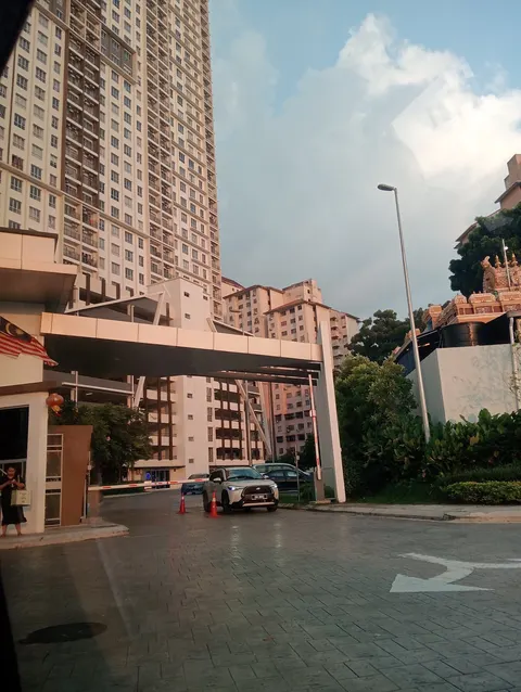Vista OUG: The entrance and driveway of a residential development, showing a vehicle at the gate, covered walkways, and high-rise apartment towers.