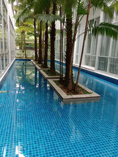 Nobleton Crest: A swimming pool with blue mosaic tiles and concrete planters holding palm trees, situated between building wings.