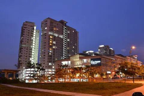 Cova Suites: A twilight view of the Cova Suites condominium complex, featuring illuminated high-rise residential towers and a lower commercial podium with a visible sign, set against a dark blue sky.
