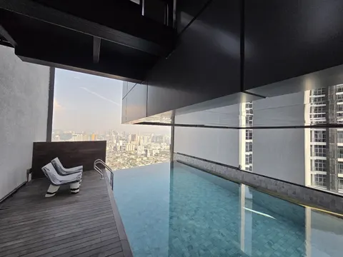 Isola KLCC: A high-level rooftop infinity pool with a wooden deck and lounge chairs, overlooking a sprawling cityscape.