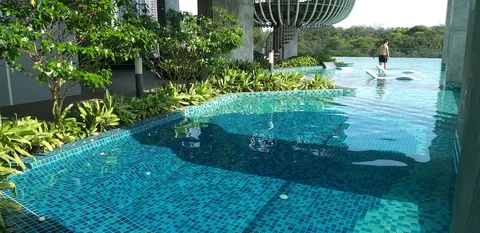 SkyLuxe On The Park @ Bukit Jalil: A swimming pool with blue mosaic tiles, surrounded by greenery and building structures, with a person standing in the water.