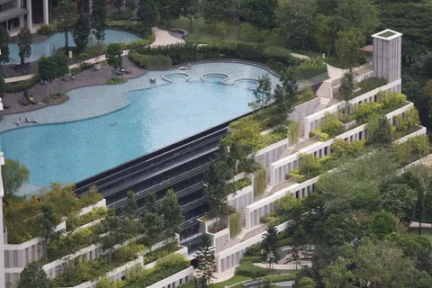Park Regent by the Water: An elevated view of a large outdoor swimming pool with a person swimming in it, bordered by a waterfall and landscaped terraces.