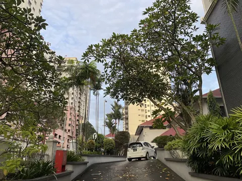 Menara Duta 1: A driveway leading to a gated residential entrance, lined with trees and low walls, with high-rise buildings visible in the background.