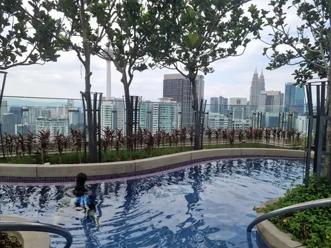 Regency Tower: An outdoor swimming pool with a person swimming in it, surrounded by trees and plants, offering a view of the city skyline in the background.