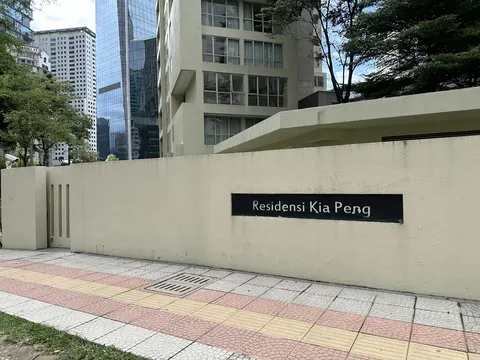 Residensi Kia Peng: A street view of a cream-colored boundary wall featuring a black nameplate, with the residence and surrounding urban buildings visible in the background.