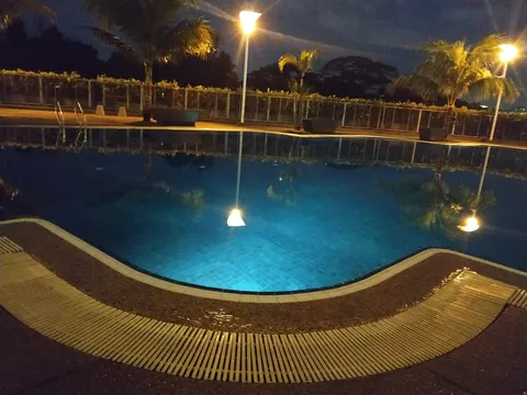 633 Residency: A swimming pool with blue tiled bottom and underwater lighting at night, surrounded by a deck and a fence with trees beyond.