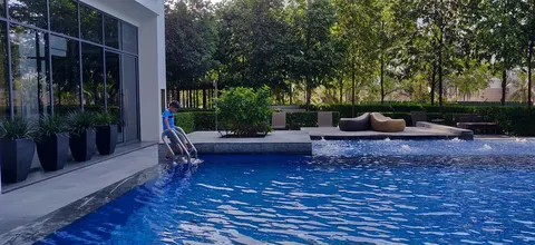 Rimbun @ Embassy Row: A swimming pool area with a person climbing up the ladder, surrounded by lounge chairs, potted plants, and a glass-walled building.
