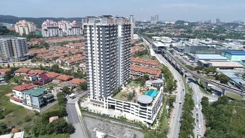Denai Sutera: An aerial photograph of a completed high-rise residential tower with a podium, set within a landscaped neighborhood featuring terraced houses, roads, and a railway line with a passing train.