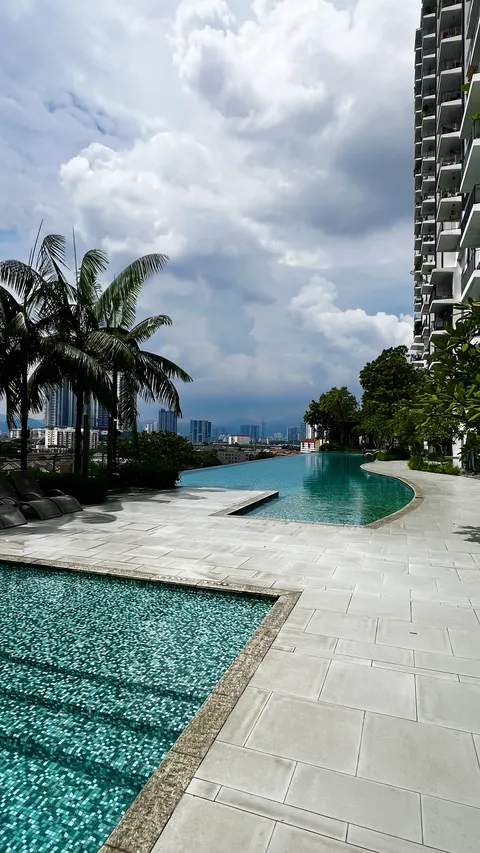 Verdana @ North Kiara: A view of an infinity pool and pool deck at a high-rise residential complex with palm trees and a city skyline in the background.