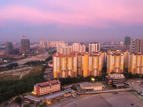 D'Latour: A high-angle aerial view of a residential development featuring multi-story towers with yellow, white, and brown facades and red-tiled roofs, set against a city skyline at dusk.