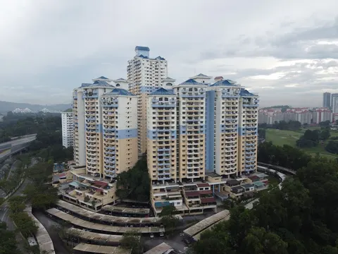 Vista Komanwel: Aerial view of a residential apartment complex with multiple high-rise towers featuring cream and blue facades and blue roofs, situated near a highway and green park area.