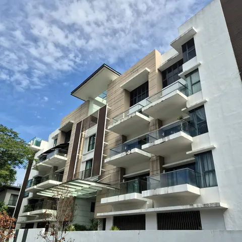 Identiti U-Thant: Low-angle view of the exterior facade of a modern condominium building with balconies, looking up against a blue sky with scattered clouds.