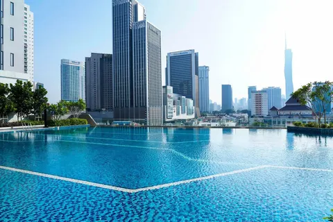 Sentral Suites: A large, blue infinity swimming pool on a rooftop with a backdrop of a modern city skyline featuring several high-rise towers and a very tall spire in the distance.